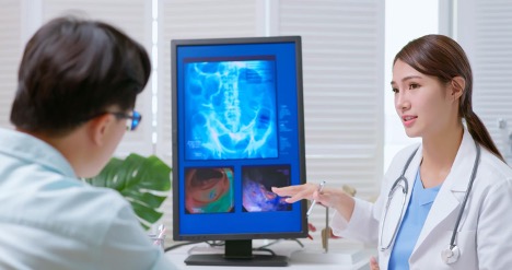 Female doctor explaining a colonoscopy to a patient with a colon model in a PC screen