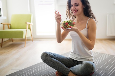 A woman sits on the floor, eating vegetables and fruits to improve her health and digestive system.